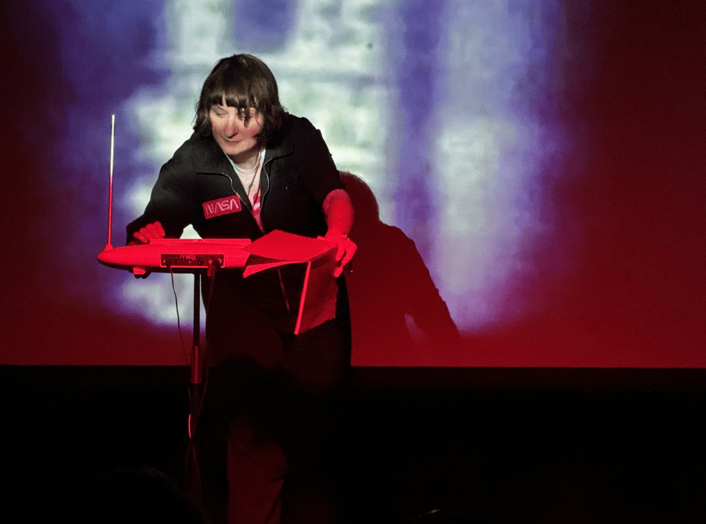 Ela Orleans performs Night Voyager. She is wearing a black Nasa boiler suit and plays the theremin. 